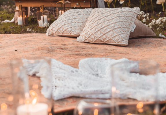 outdoor picnic with candles, pillows, pink blanket and flowers in the background
