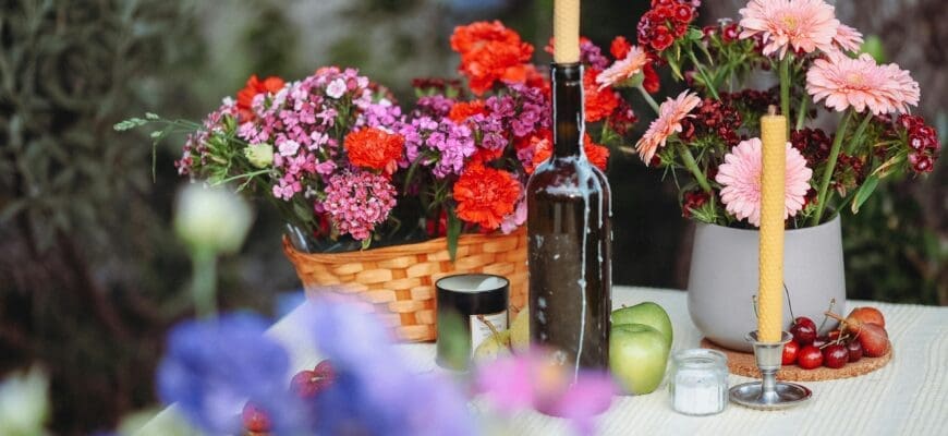 A Table with a Basket Full of Flowers, a vase of Flowers, a Candlestick, and a Wine Bottle with a Candle in it